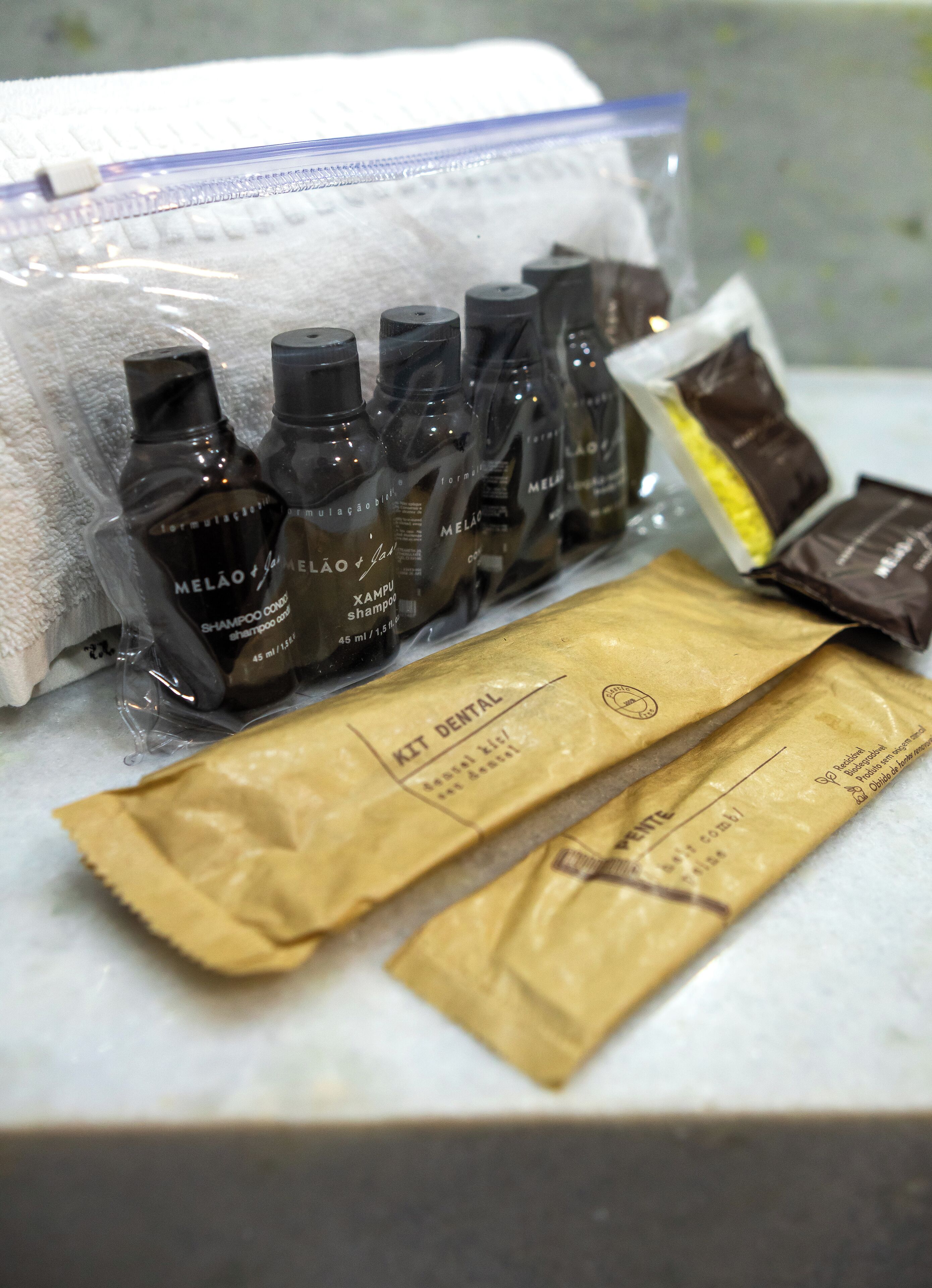 A bathroom counter with toiletries including bottles of shampoo and a dental kit.