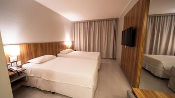 Une chambre d’hôtel avec deux lits, un téléviseur fixé au mur, une table de chevet avec un téléphone et un panneau en bois sur le mur.
