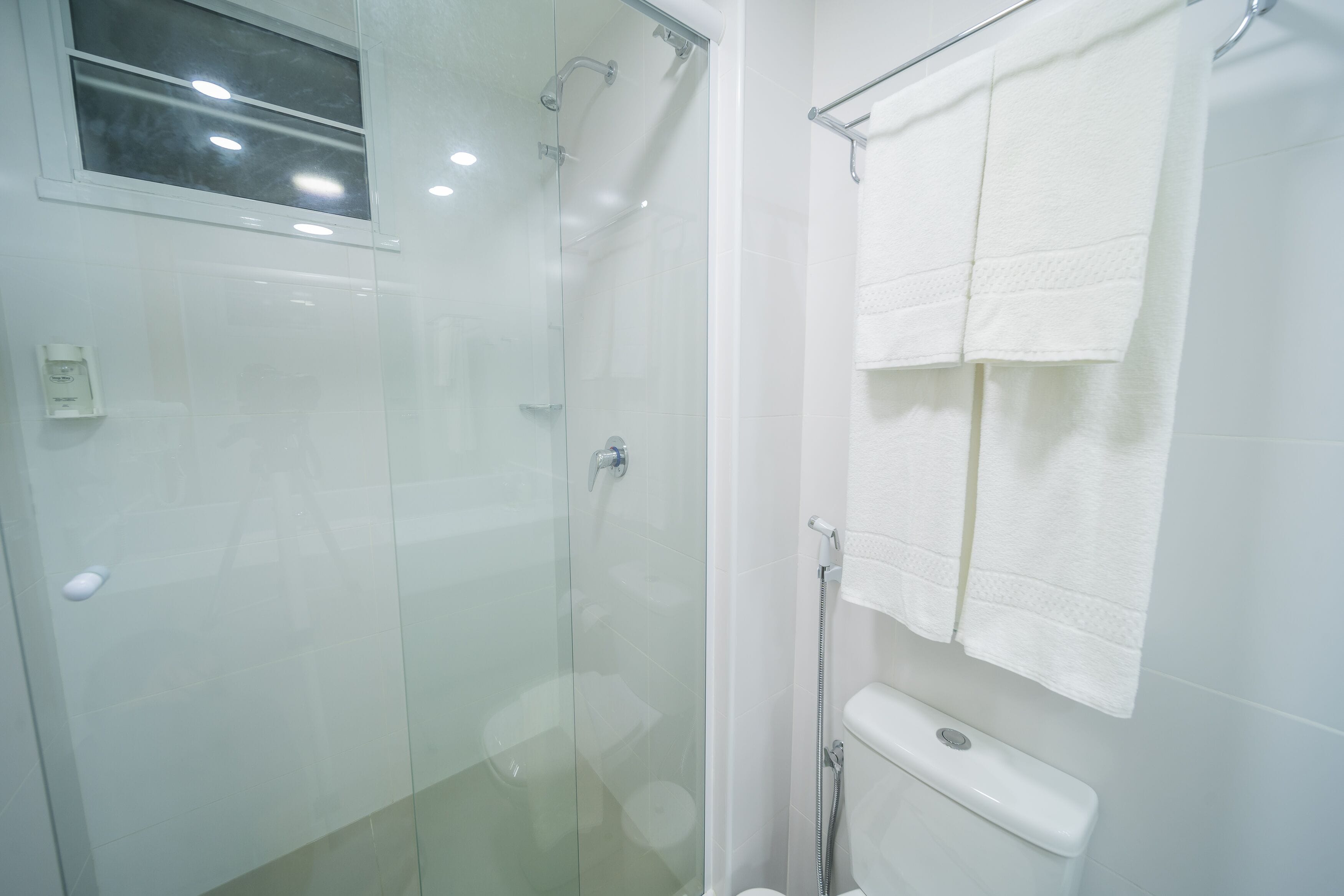 Un bagno moderno con box doccia in vetro, un water con porta asciugamani e un asciugamani elettrico a muro.