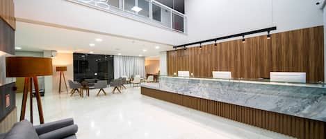 A modern hotel lobby with a reception desk, seating area, and a second-floor balcony.