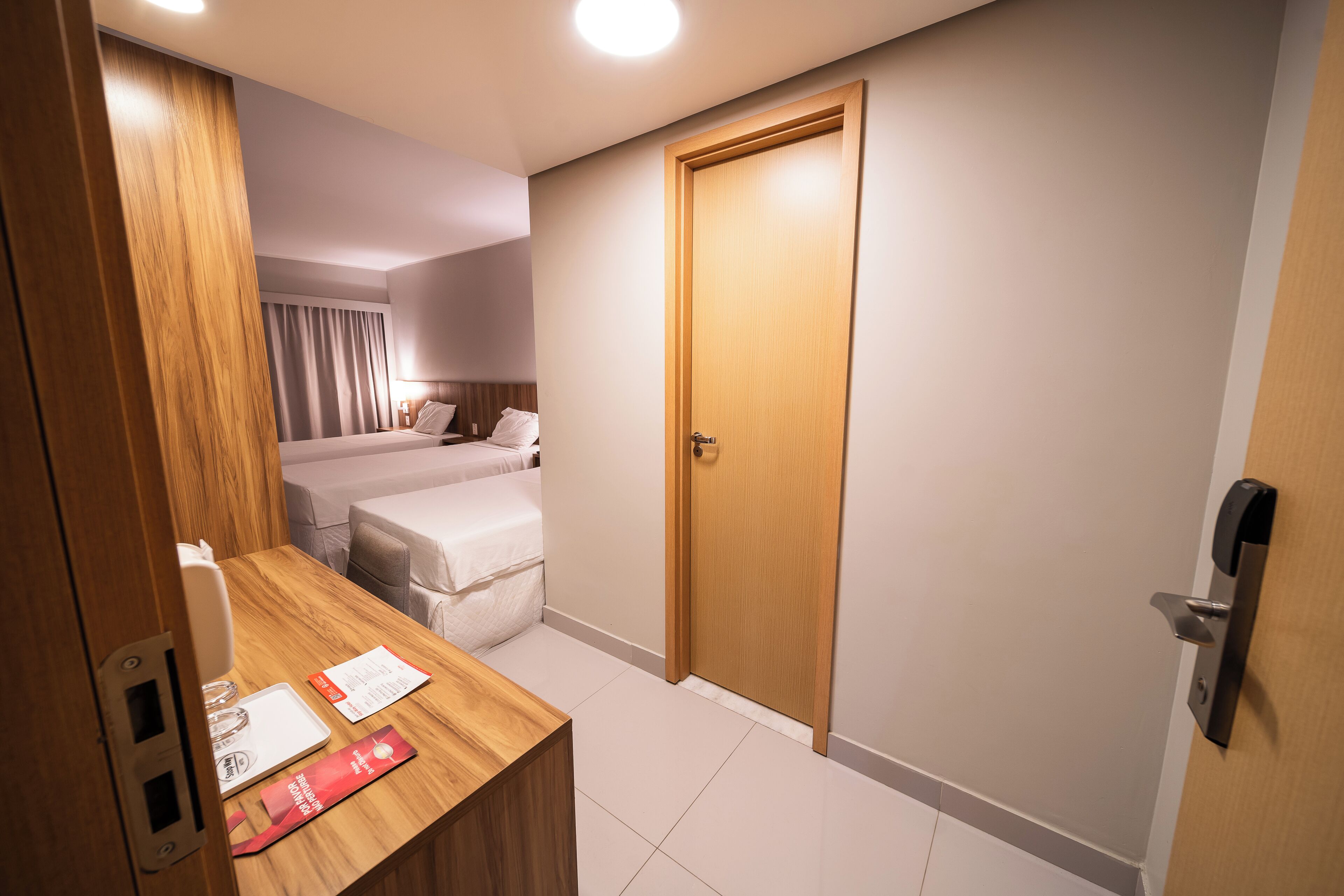 Ein Hotelzimmer mit Holzschreibtisch, einem Bett, einer Tür und einem durch einen Vorhang einsehbaren Badezimmer.
