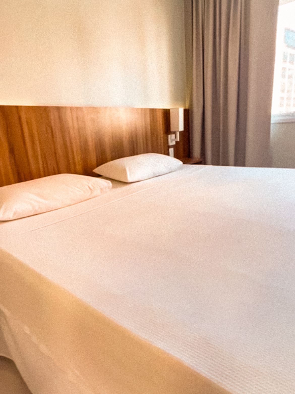 Cama bem arrumada com cabeceira de madeira e travesseiro branco.