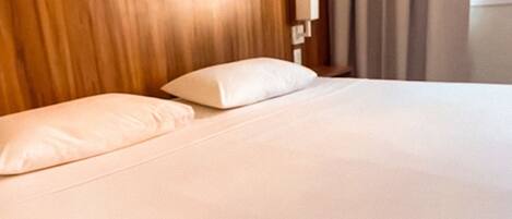 Una cama bien hecha con cabecera de madera y almohada blanca.
