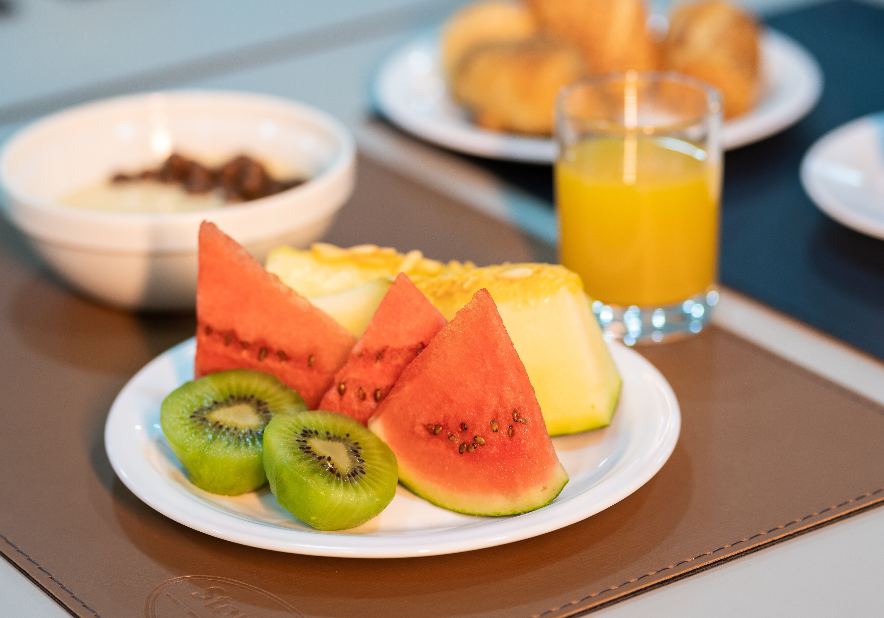 Un desayuno con una ensalada de sandía, kiwi y queso, un vaso de jugo de naranja y un tazón de cereal.
