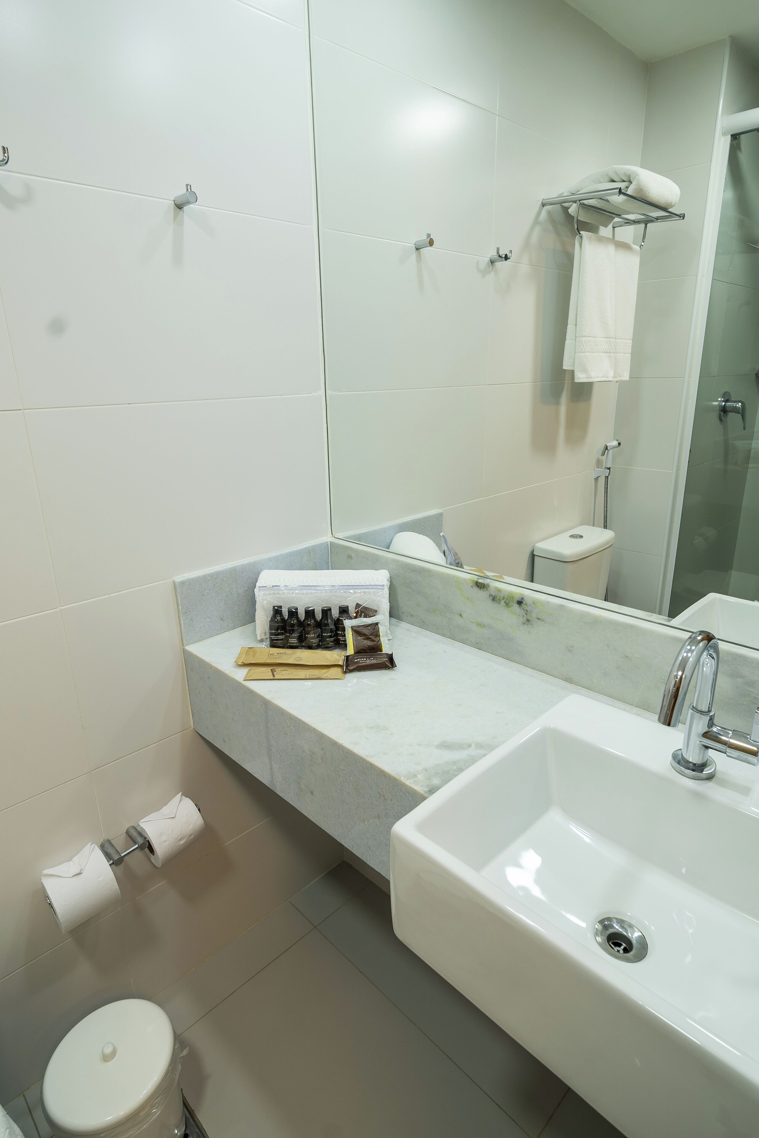 A modern bathroom with a large sink, mirror, and toilet. There are toiletries on the counter and a towel rack above the mirror.