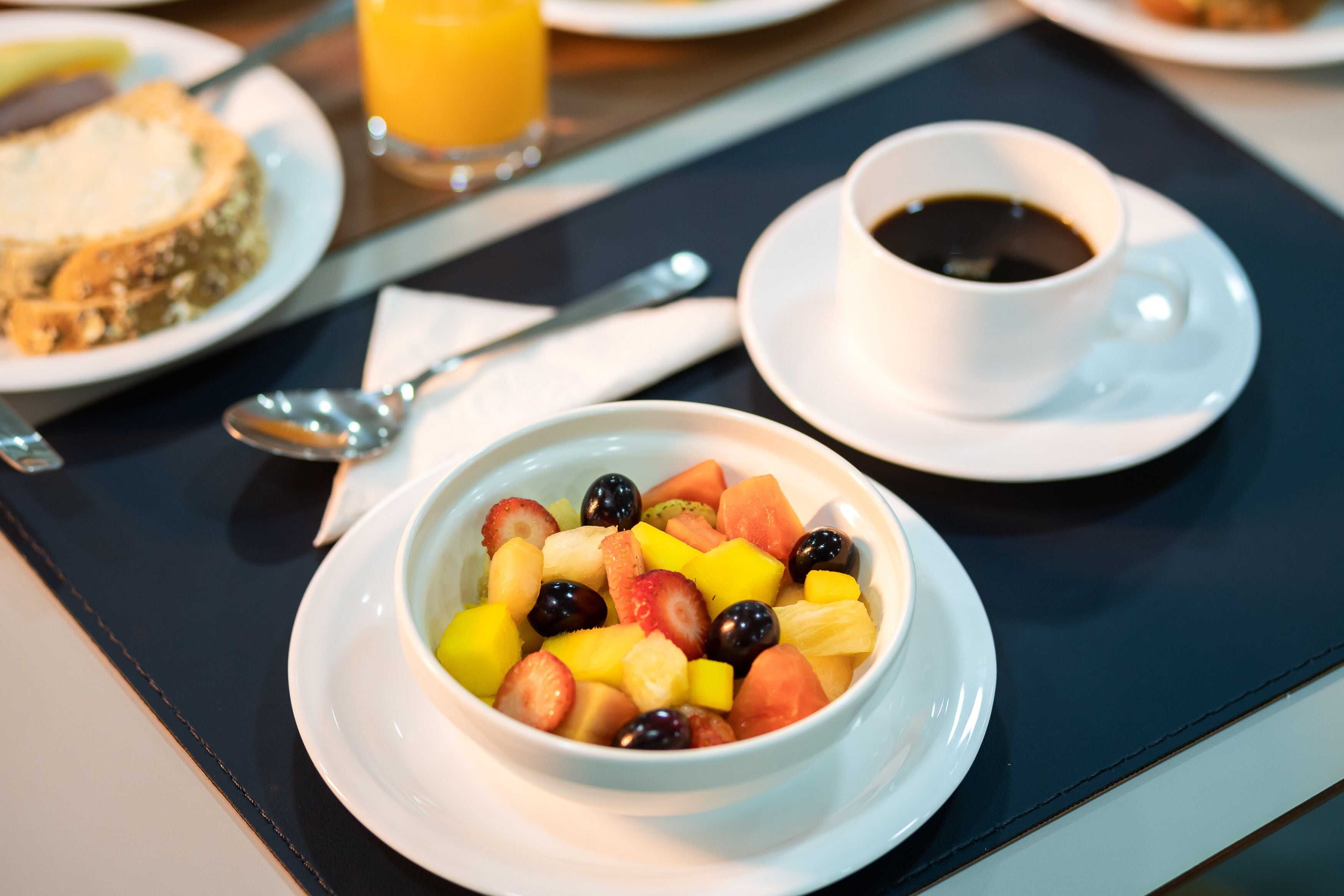 Mesa de café da manhã com uma tigela de frutas, uma xícara de café e uma fatia de torrada.