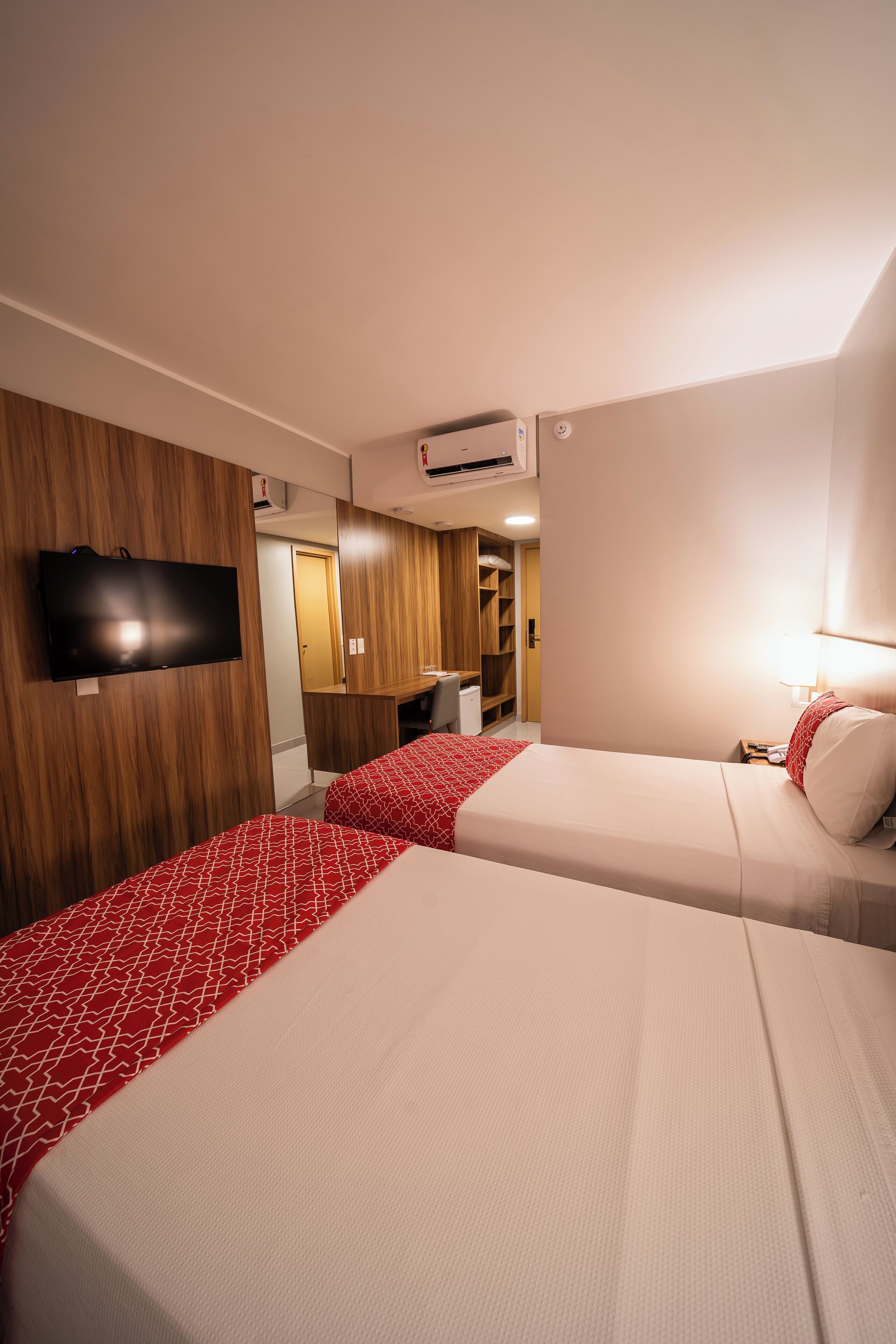 Een hotelkamer met twee bedden, een aan de muur bevestigde televisie en een spiegel.