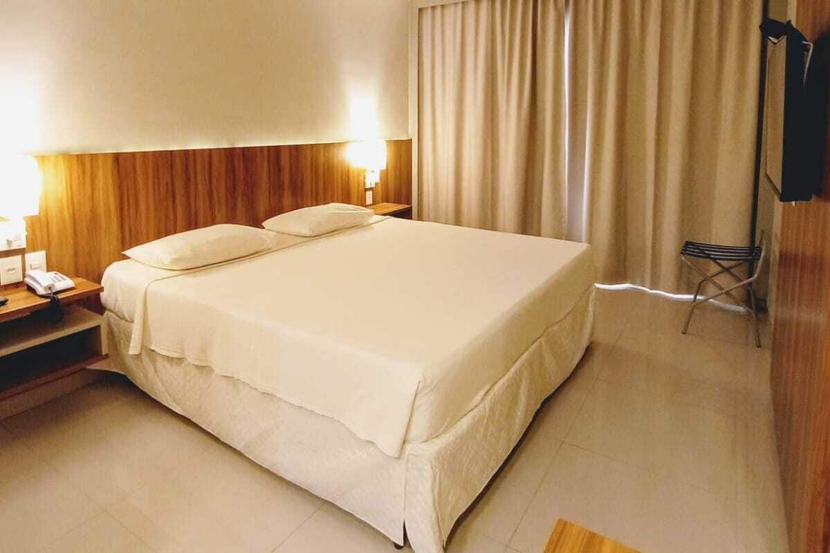 A hotel room with a large bed, a desk with a lamp, a chair, and a TV mounted on the wall.