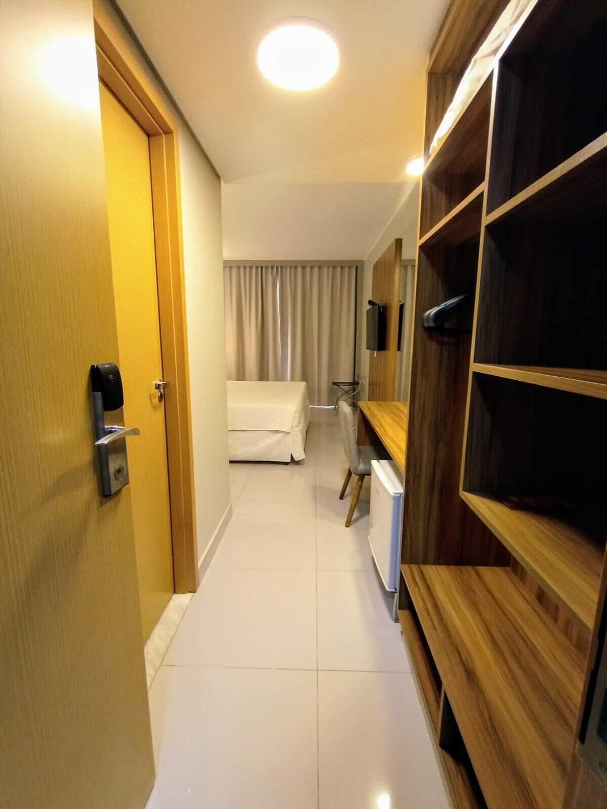 Quarto de hotel com guarda-roupa de madeira, uma cama, uma escrivaninha e uma televisão.