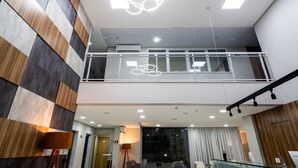 A modern hotel lobby with a checkered wall pattern, a glass railing with Olympic rings, and a staircase to an upper level. - Stop Way Hotel Fortaleza (Fortaleza)