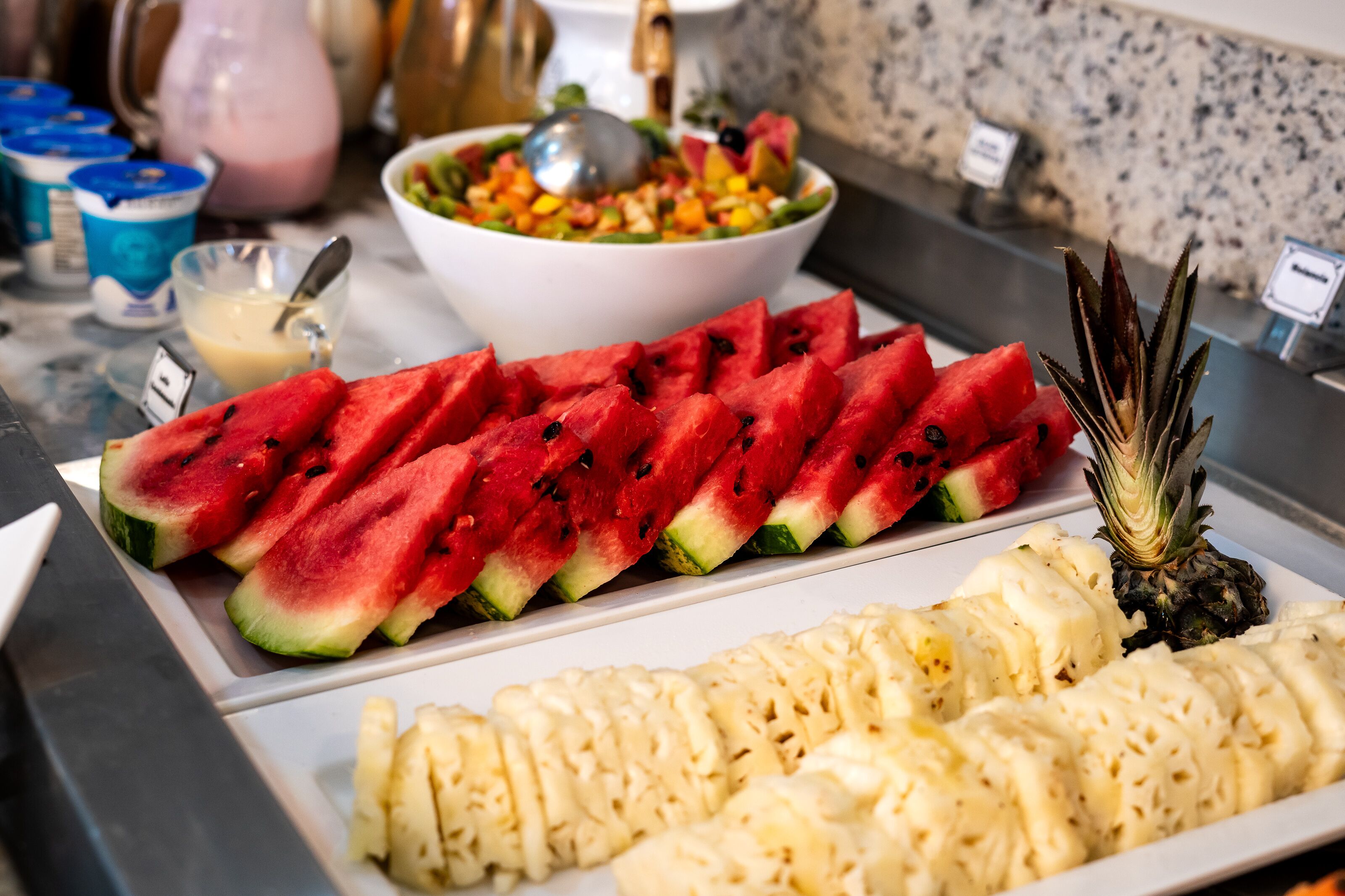 A buffet with sliced watermelon, pineapple, and a mixed fruit salad.