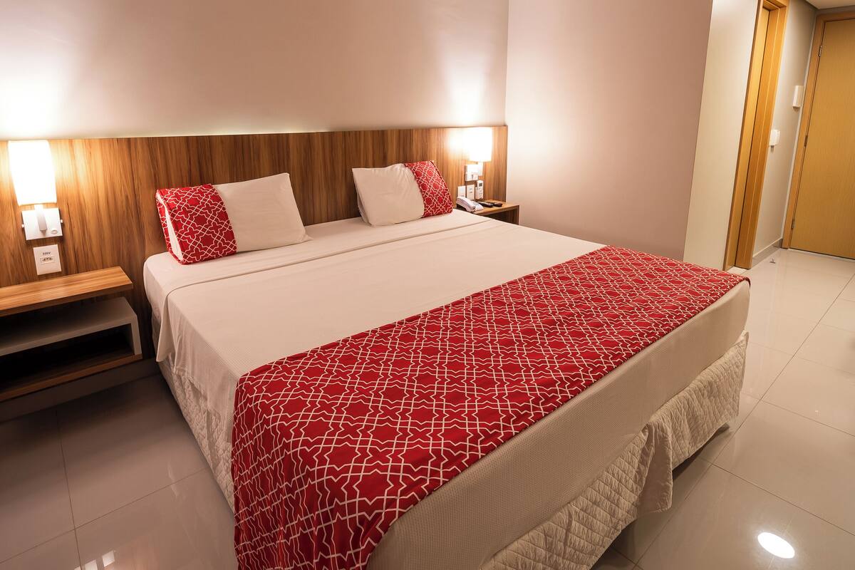 A hotel room with a large bed, a wooden headboard, bedside lamps, and a door to the right.