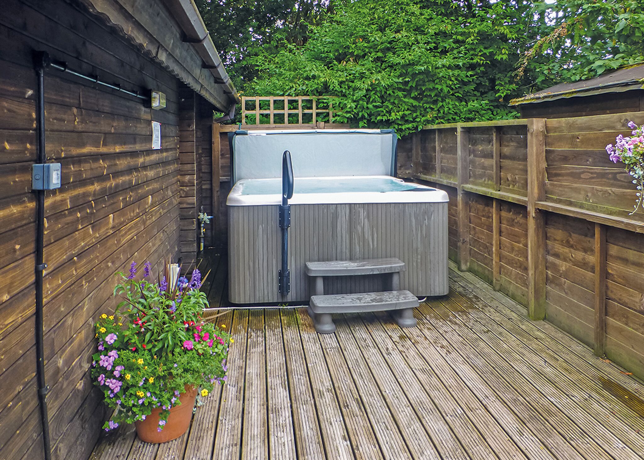 Une terrasse en bois avec un jacuzzi, une clôture en bois et un pot de fleurs.