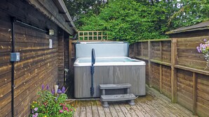 A wooden deck with a hot tub, a wooden fence, and a potted plant with flowers. - Studio timber lodge with one double. (Kentisbeare, Nr Cullompton)