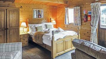 Une chambre dans une cabane en bois, avec un lit, des tables de chevet, une chaise et une fenêtre avec des rideaux.