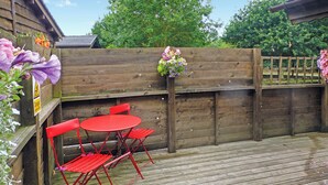 A wooden deck with a red metal table and chairs, a wooden fence, and a flower pot with flowers. - Studio timber lodge with one double. (Kentisbeare, Nr Cullompton)