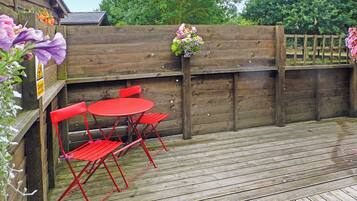 Une terrasse en bois avec une table et des chaises en métal rouge, une clôture en bois et un pot de fleurs.