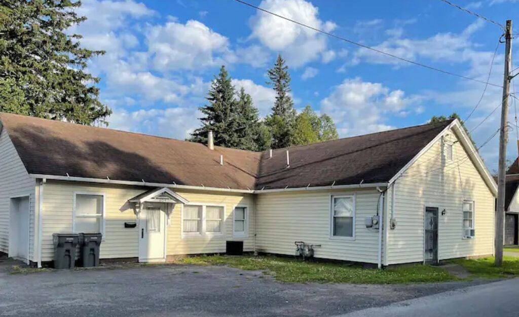Un bâtiment à deux étages, doté d’un toit en pente, d’un porche à l’avant et d’un garage.