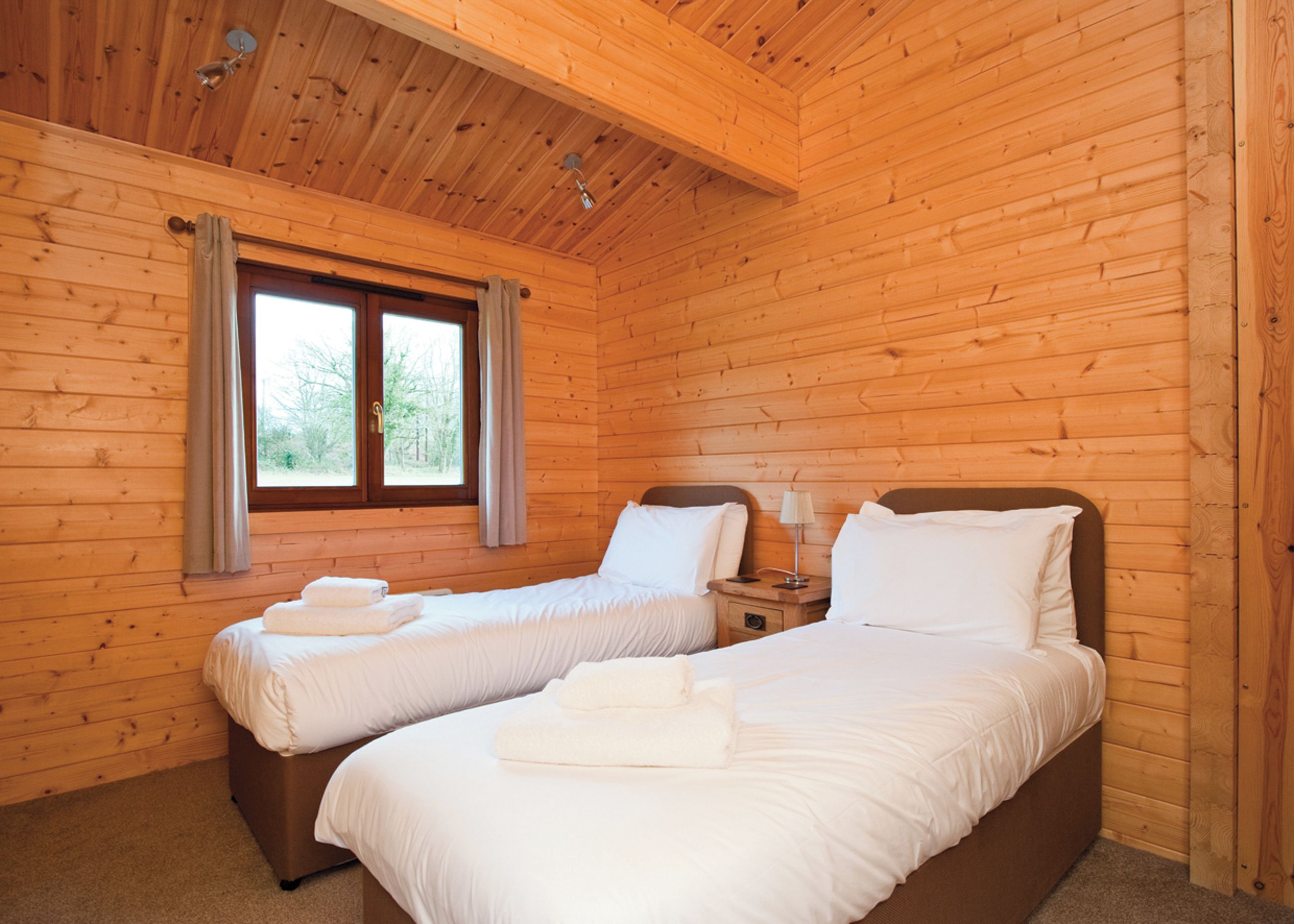 A wooden cabin bedroom with two beds, a window, and a ceiling light.