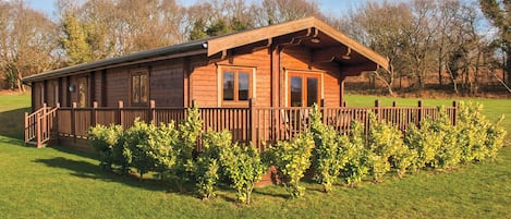 A wooden cabin with a porch, surrounded by a well-maintained lawn and trees.
