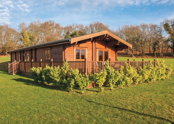 A wooden cabin with a porch, surrounded by a well-maintained lawn and trees.