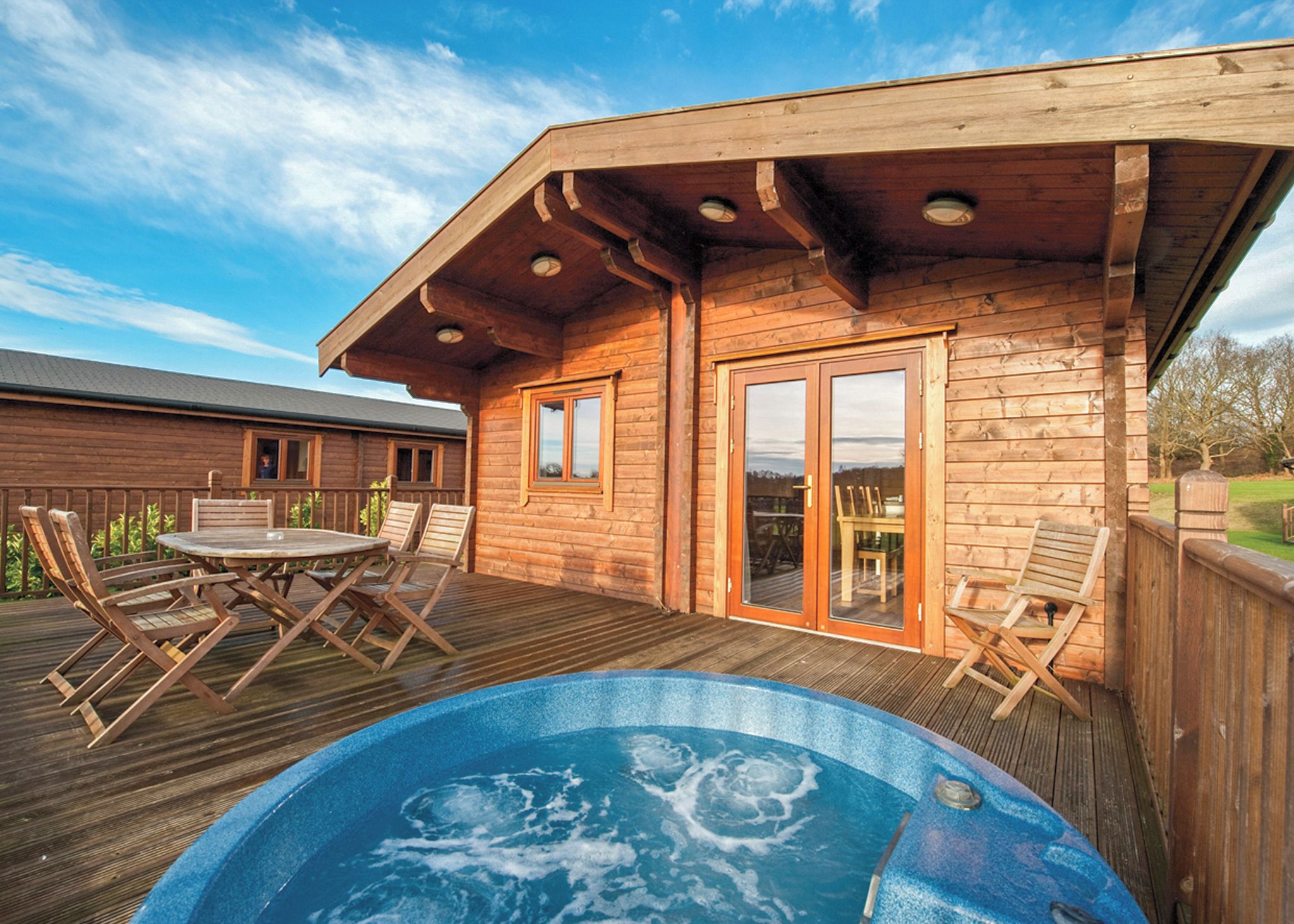 A wooden deck with a hot tub, outdoor seating, and a view of a forest.