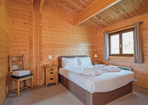 A wooden cabin room with a bed, bedside tables, a chair, and a window.