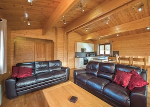 A cozy cabin interior with two leather sofas, a wooden coffee table, a kitchen area, and a dining table.