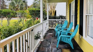 Eine Veranda mit weißer Geländer, Steinboden und türkisfarbenen Stühlen.