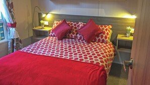 A bed with a polka dot pattern, two red pillows, bedside tables with lamps, and a window with curtains.