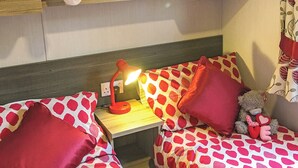 A bedroom with two beds, each with red and white polka dot bedding, a bedside table with a lamp, and a teddy bear on one bed.