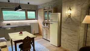 Una cucina compatta con tavolo e sedie, un frigorifero e una finestra che si affaccia su una zona verde.
