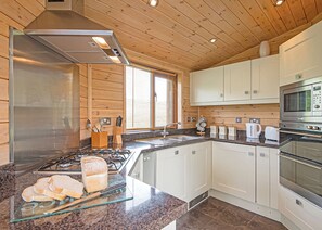 A modern kitchen with a stainless steel range, white cabinets, a granite countertop, and a large window with blinds. - Superior and stunning stylish pine lodge. (Whitfield, Hexham)