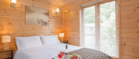 Une chambre aux murs lambrissés, avec un lit, des lampes de chevet, une fenêtre avec des stores et un plateau contenant de la nourriture et des boissons, posé sur le lit.