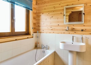 Une salle de bain aux murs lambrissés, avec une fenêtre, un lavabo et une douche.