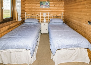 Une chambre de style cabane en bois, avec deux lits simples, une table de chevet avec une lampe et une fenêtre avec des rideaux.