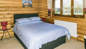 Un dormitorio de cabaña de madera con una cama, dos mesitas de noche, un radiador y una ventana con cortinas.
