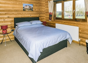 Ein Schlafzimmer einer Holzhütte mit einem Bett, zwei Nachttischen, einem Heizkörper und einem Fenster mit Vorhängen.