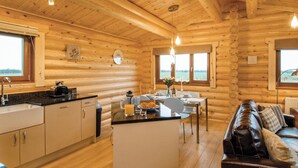 Interior de una cabaña de troncos con cocina, comedor y un sofá de cuero.