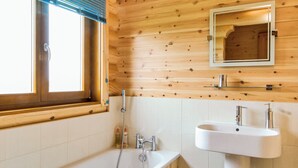 Un baño con paneles de madera, una ventana, un lavabo y una ducha.