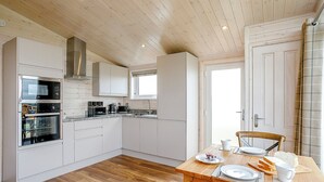 Une cuisine moderne avec des meubles blancs, un four encastré et un coin repas comprenant une table et des chaises en bois.
