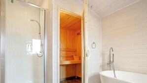 Une salle de bain dotée d’une douche à parois de verre, d’un sauna en bois et d’une baignoire sur pied.