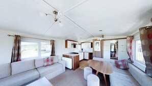 A compact RV interior with a kitchenette, a sofa, a dining table, and a ceiling fan. - The Gold Plus 2 caravan (pet) is 12ft wide with one double and one twin. (Clarach Bay, Nr Aberystwyth)