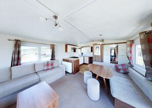 Ein kompaktes Wohnmobil-Interieur mit Küchenzeile, einer Sitzecke, einem Esstisch und einem Deckenventilator.