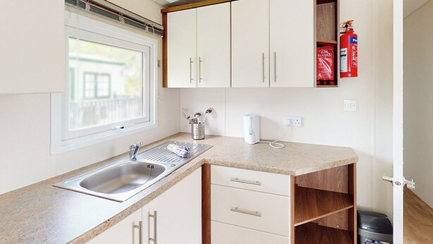 A kitchen with a sink, countertop, cabinets, a window, and a fire extinguisher. - The Gold Plus 2 caravan (pet) is 12ft wide with one double and one twin. (Clarach Bay, Nr Aberystwyth)