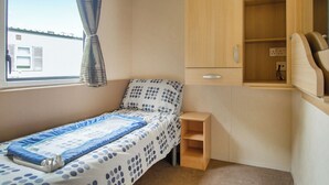 A bedroom with a single bed, a small wooden cabinet, and a window with curtains. - The Gold Plus 2 caravan (pet) is 12ft wide with one double and one twin. (Clarach Bay, Nr Aberystwyth)