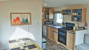 A compact kitchenette with a stove, sink, and wooden cabinets. - The Gold Plus 2 caravan (pet) is 12ft wide with one double and one twin. (Clarach Bay, Nr Aberystwyth)