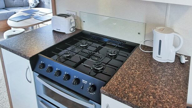 A compact kitchen with a gas stove, oven, and a coffee maker on the countertop. - The Gold Plus 2 caravan (pet) is 12ft wide with one double and one twin. (Clarach Bay, Nr Aberystwyth)