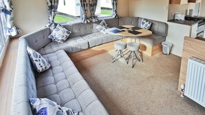 A caravan interior with a sofa set, a round table, and a kitchen area. - The Gold Plus 2 caravan (pet) is 12ft wide with one double and one twin. (Clarach Bay, Nr Aberystwyth)