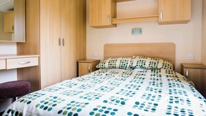 A bedroom with a bed, a nightstand, a dresser, and a mirror. - The Gold Plus 2 caravan (pet) is 12ft wide with one double and one twin. (Clarach Bay, Nr Aberystwyth)